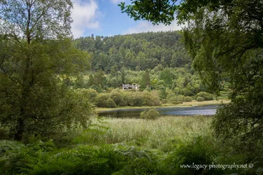 $House in the Irish countryside across Glendalough lake - framed by trees.webp