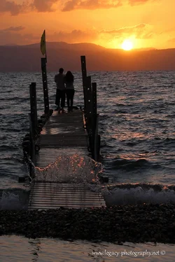$Couple standing on a dock on the Kinneret at sunset with wave splash - 2.webp