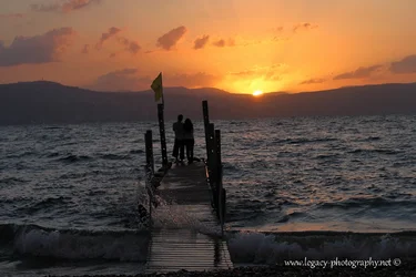$Couple standing on a dock on the Kinneret at sunset with wave splash - 3.webp