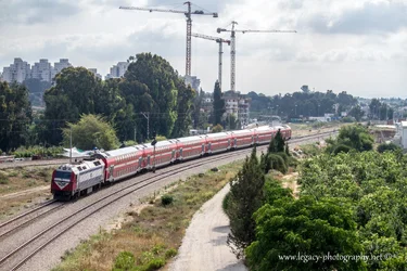 $Train on tracks - buildings trees and cranes in background.webp $Train on tracks - buildings trees and cranes in background.webp