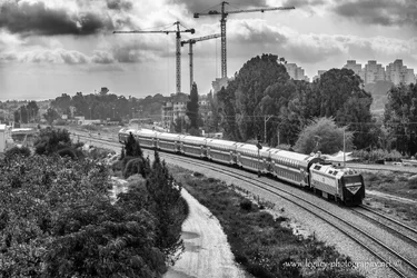 $Train on tracks - buildings trees and cranes in background - High contrast BW right to left.webp $Train on tracks - buildings trees and cranes in background - High contrast BW right to left.webp