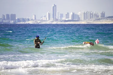 $Spear fisherman heading into ocean with speargun in hand Tel Aviv in the background - small.webp $Spear fisherman heading into ocean with speargun in hand Tel Aviv in the background - small.webp