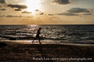 $Silhoutted runner on the beach at sunset.webp
