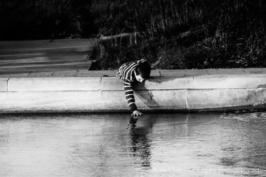 Sholom lying on banks and putting hand into stream - BW.webp