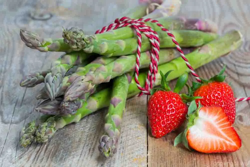 Green asparagus with strawberries on wooden